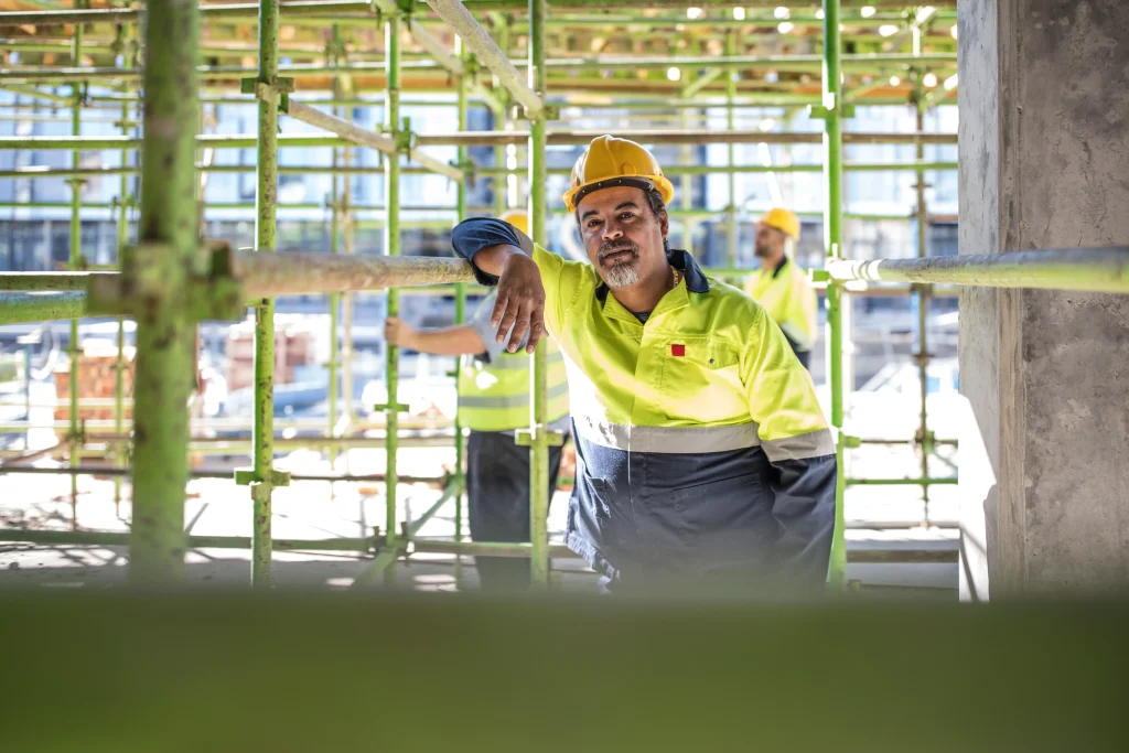 homem olha para a câmera em um canteiro de obras e ilustra a capa da reportagem sobre aluguel de ferramentas para construção. Tipos de andaimes para locação em Nova Lima: Qual escolher para seu projeto?