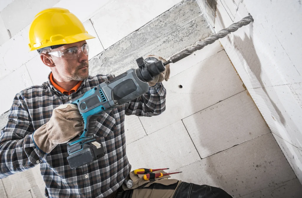 Trabalhador utilizando furadeira de impacto em parede de concreto
