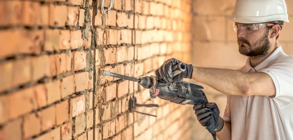 Operário perfurando parede de tijolos com furadeira elétrica