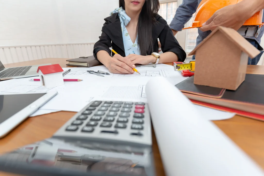 Compradora calculando valores de equipamentos para obra com planilhas e projetos.