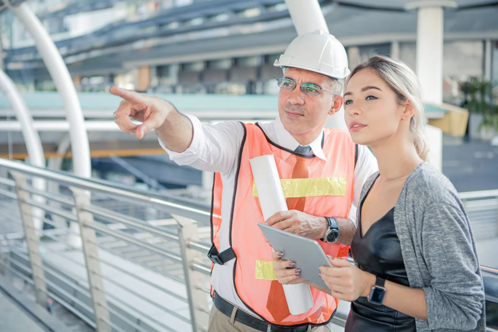 Engenheiro sênior orientando arquiteta durante análise de equipamentos para obra.