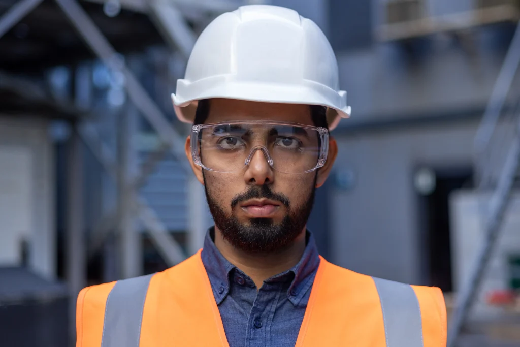 Engenheiro com capacete branco e óculos de proteção em obra industrial. EPI na construção civil